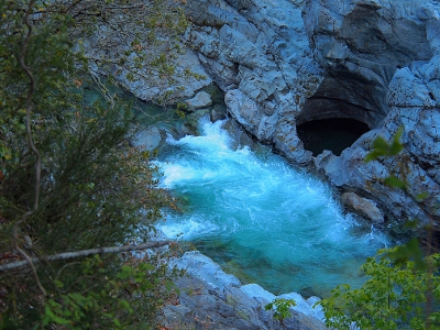 [A turbulent section of river beside a circular opening in the adjacent rock.]